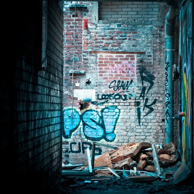 La imagen muestra un callejón con un muro con graffiti al fondo y colchones y otros objetos tirados en el suelo.