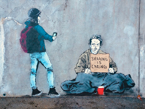 La imagen muestra a un joven grabando a un vagabundo portando un cartel que reza: “ Sharing is caring”.
