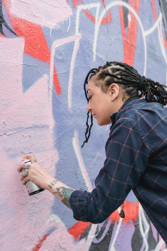 La imagen muestra a una chica pintando con aerosol un graffiti.