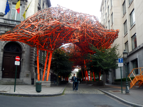 La imagen muestra una calle rodeada de árboles gigantes hechos de láminas de madera pintadas de color naranja 