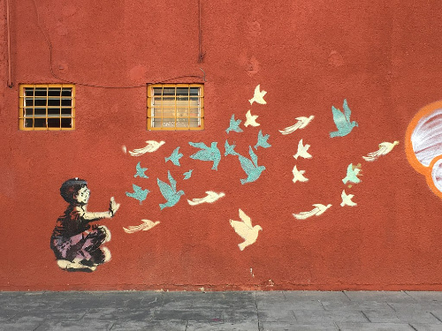 La imagen muestra un graffiti pintado con plantillas en la pared de un edificio.Muestra a un niño con pájaros