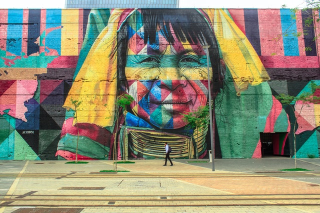 La imagen muestra una obra de arte urbano realizada en una pared muy grande y mostrando la imagen de una indígena. 