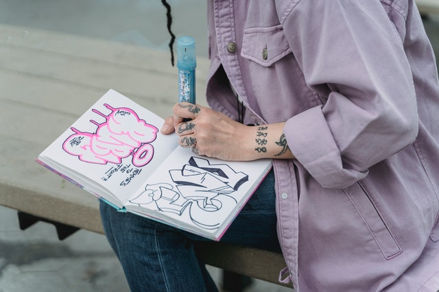 La imagen muestra a una persona diseñando su firma con graffiti (tag) en un cuaderno.