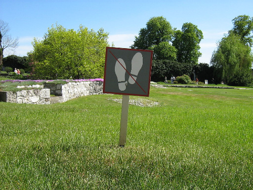 La imagen muestra un campo verde con un cartel de prohibido pisar.