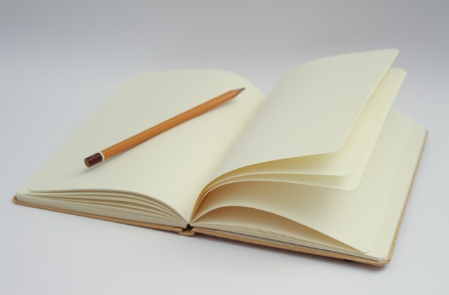 La imagen muestra un libro abierto con sus páginas vacías sobre el que está apoyado un lápiz.
