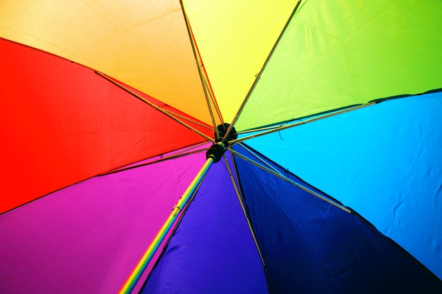 La imagen muestra un paraguas con los colores del arcoiris visto desde la parte interna del mismo.