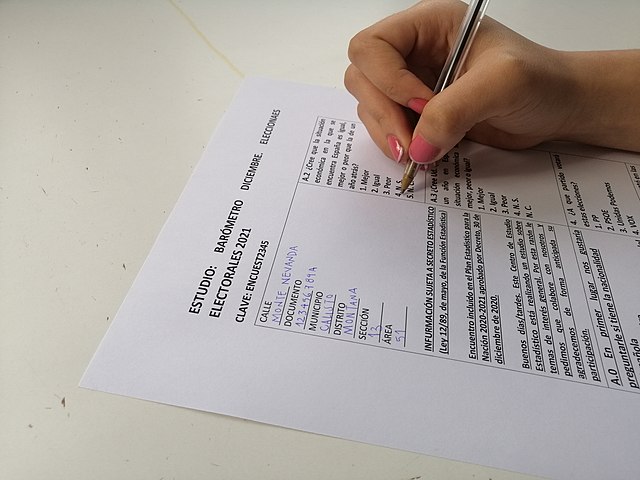 La imagen muestra una persona rellenando una encuesta en papel