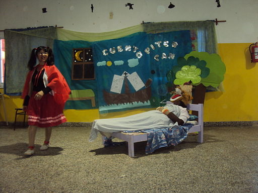 Escena de la representación del cuento de Caperucita en la que aparece el lobo en la cama y Caperucita acercándose.