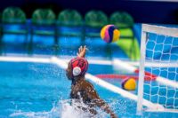 Portera de waterpolo intenta detener una pelota. LLeva un gorro rojo