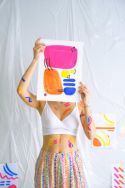 Aparece una mujer con un dibujo que le tapa la cara, en el dibujo aparece unos dibujos en tonos rosas, amarillos y azules. Además tienen como unas dobles pintadas en varios sitios del cuadro en negro.