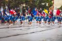 Aparecen un grupo de chicas con un uniforme azul portando banderas y desfilando.