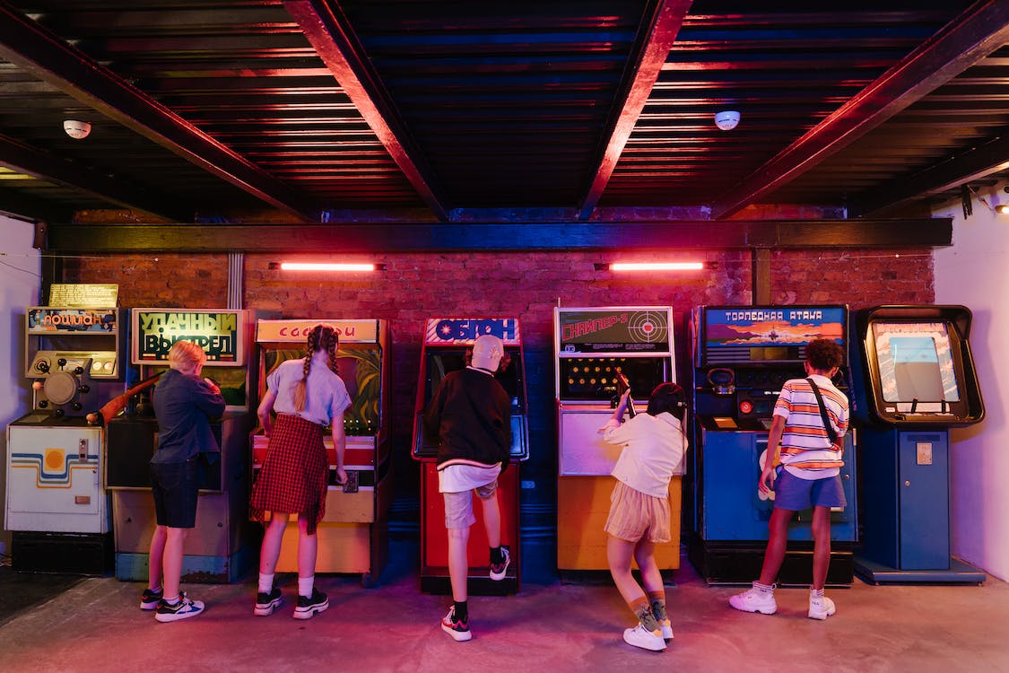 La imagen muestra unos niños de espalda jugando a videojuegos en un local comercial. 