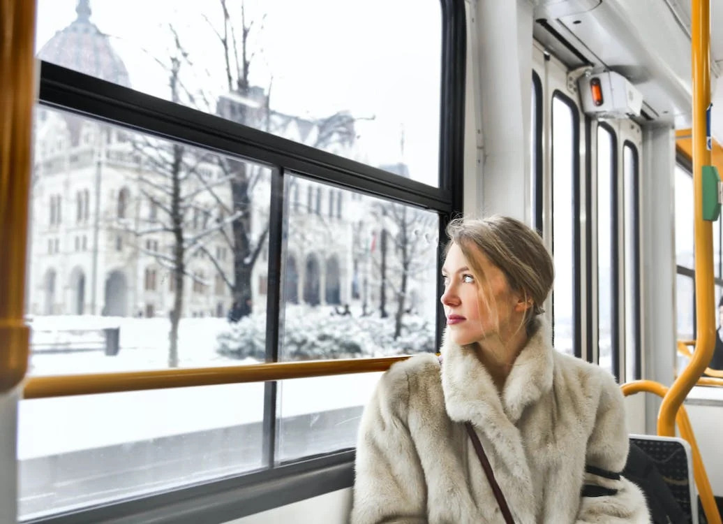 La imagen muestra una mujer sentada viajando en transporte público mientras mira el paisaje a través de la ventana. 