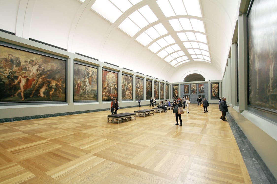 La imagen muestra una sala de un museo en la que hay cuadros pintados. Delante de la obra de arte hay personas observando y echando fotos a esas obras artísticas. 
