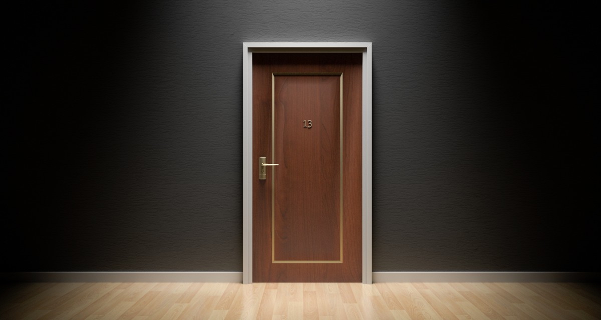 En la imagen puedes ver una puerta de madera con el número 13 en un pasillo negro