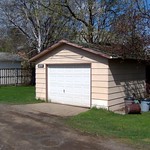 En la imagen puedes ver un pequeño garaje, con un tejado de dos aguas, en el exterior del jardín de una casa