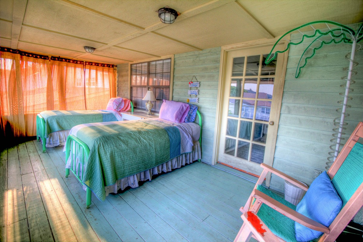 En la imagen puedes ver una habitación pintada de color verde claro y que contiene dos camas y un sillón. Además, contiene una gran ventana que da al exterior con una cortina de color naranja