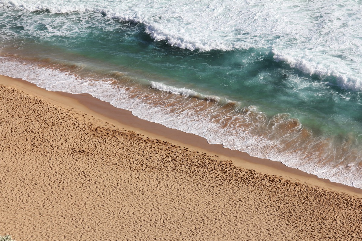 En la imagen puede verse la orilla del mar con algunas olas y arena