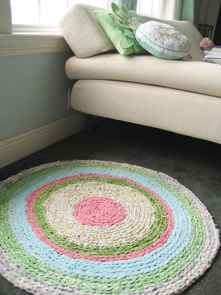 En la imagen puedes ver un sofá de lado del que se ve solo una parte y una alfombra redonda a rayas de colores en el suelo