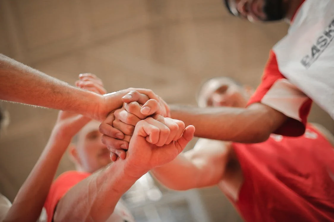 La imagen muestra a un grupo de personas apilando en el centro las manos con el puño cerrado. 