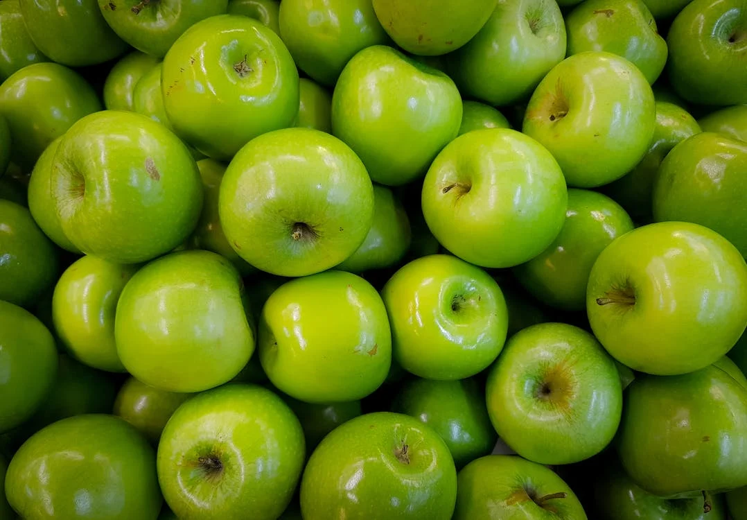 La imagen muestra un primer plano de manzanas verdes brillantes. 