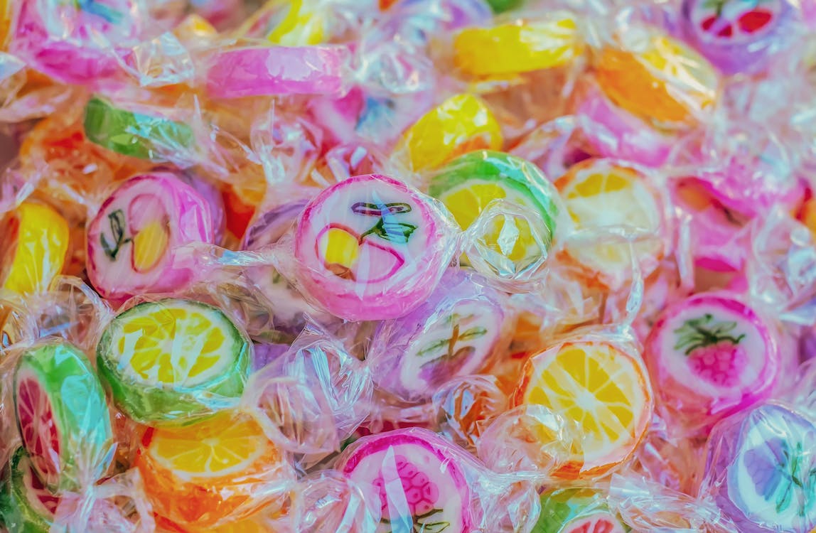 La imagen muestra un primer plano de una gran cantidad de caramelos envueltos. Los caramelos son de colores vivos rosas, amarillos, rojos, verdes y blancos.