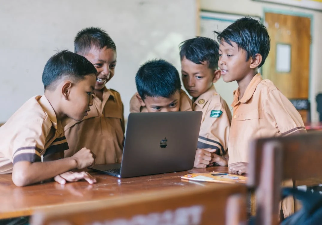La imagen muestra a cinco niños viendo un ordenador. 