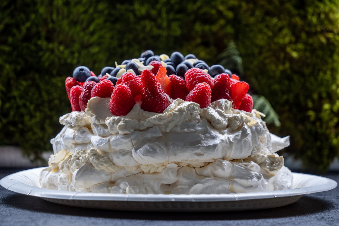 La imagen muestra una tarta hecha de nata decorada con frutos rojos, fresa, frambuesas, arándanos y coco en láminas.