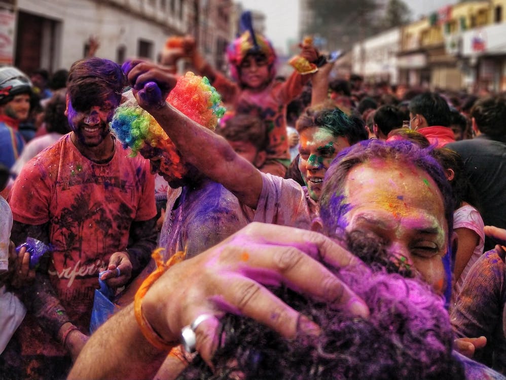 La imagen muestra a un grupo de personas en la calle disfrutando del festival de colores en la India llamado Holi Festival. Las personas se lanzan unas a otras polvos de colores llamativos.  