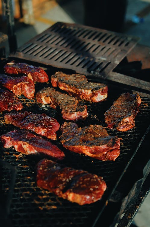 La imagen muestra una plancha de barbacoa sobre la que hay varios trozos de carne.