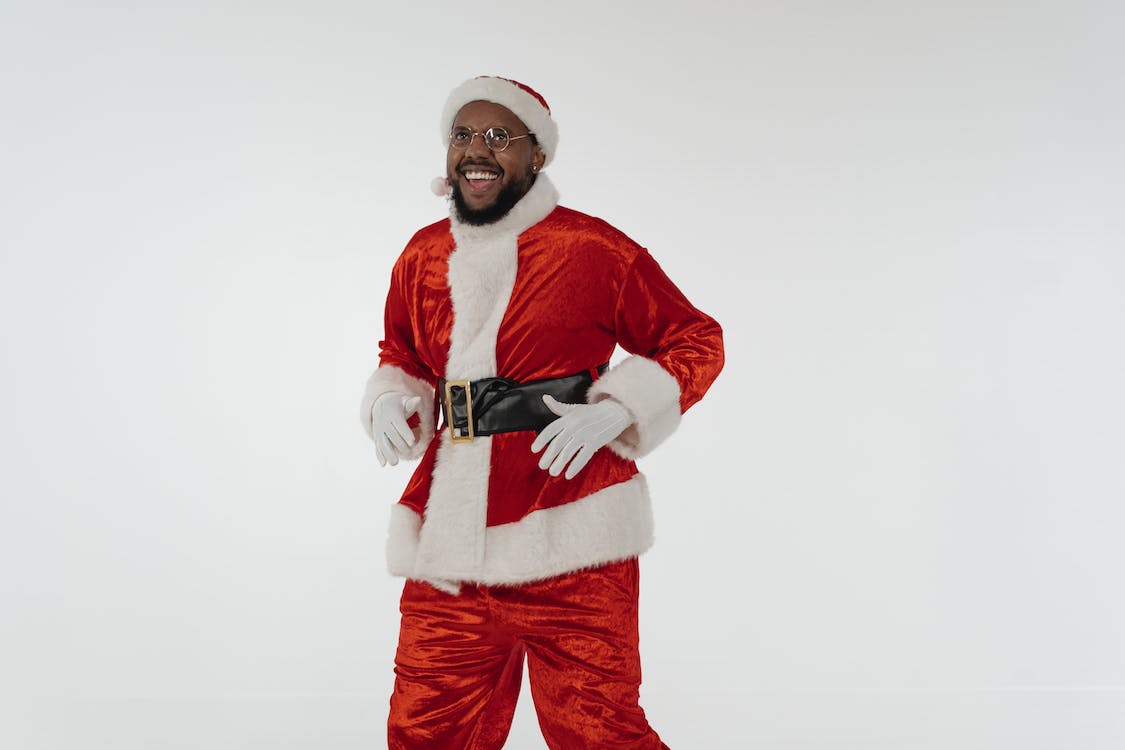 La imagen muestra a un hombre de color con barba y gafas sonriendo llevando un traje de Papá Noel.