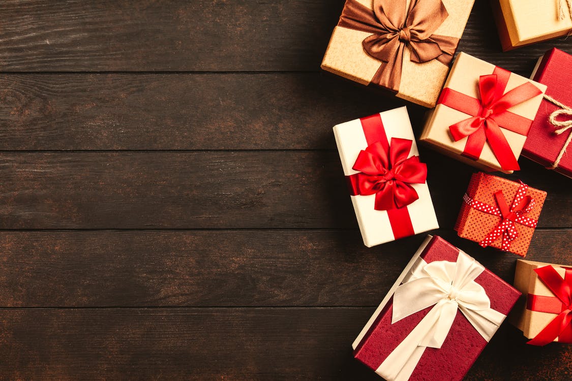 La imagen muestra ocho cajas de regalos navideños decorados con lazos rojos, todos de diferentes tamaños sobre una mesa de color madera oscura. 