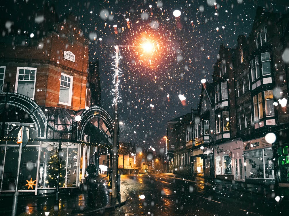 La imagen muestra una calle iluminada de noche nevando. 