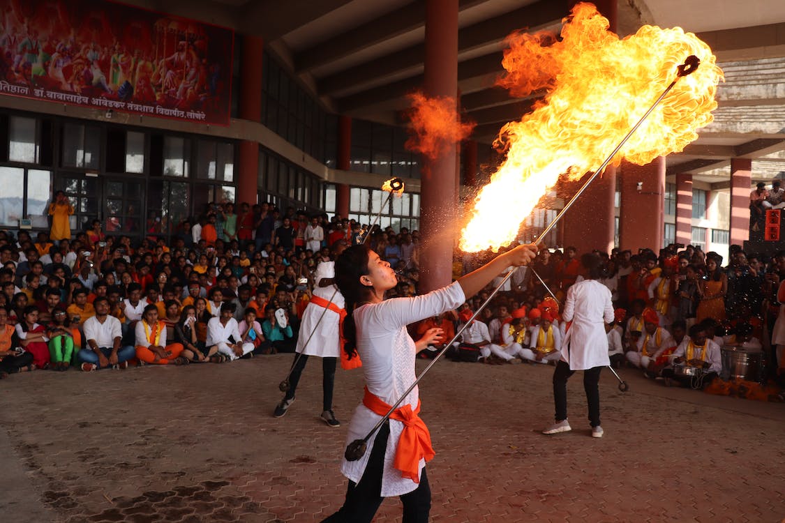 La imagen muestra a dos mujeres de la India escupiendo fuego en un espectáculo callejero durante un festival alrededor de personas.