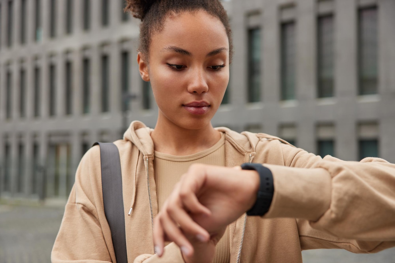 La imagen muestra a una mujer con sudadera marrón mirando su reloj de pulsera de color negro de la mano izquierda. 