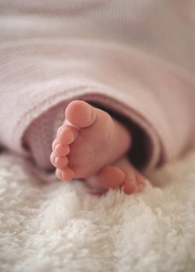 Pies de bebé sobre manta blanca de aspecto suave.