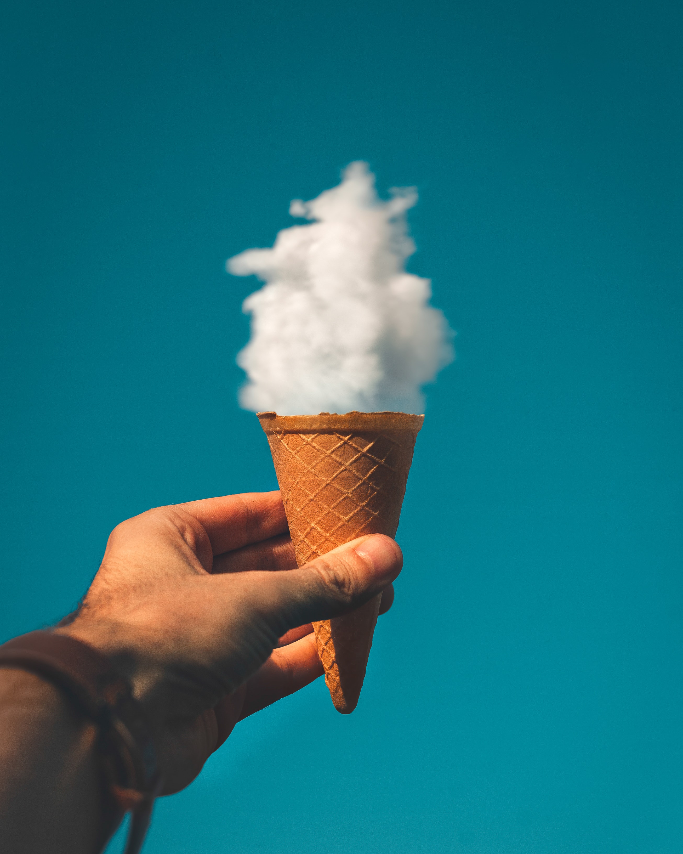 Mano sujetando un cucurucho de helado haciéndolo coincidir con una nube sobre él.