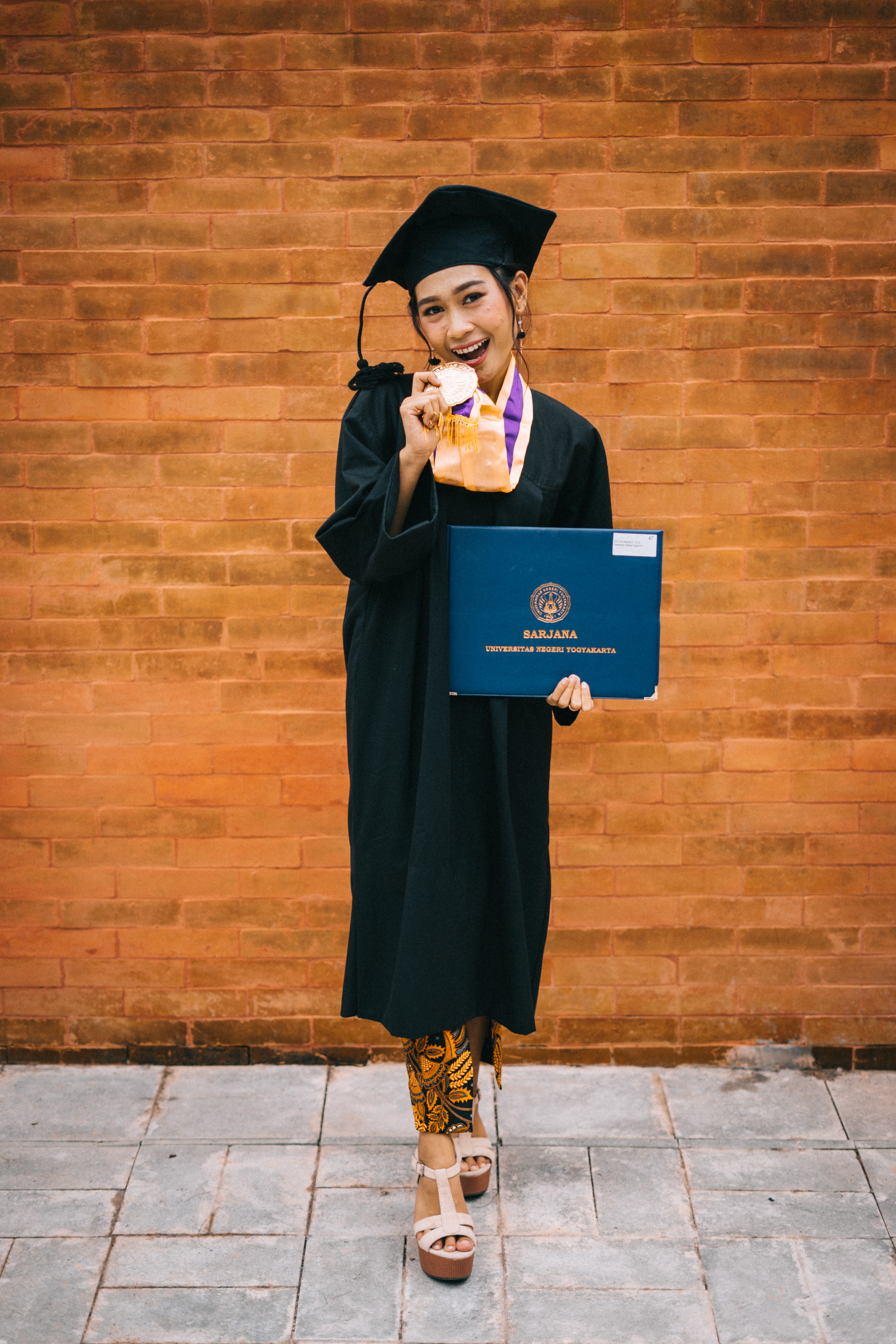 Mujer con toga negra y gorro de graduada sosteniendo un diploma universitario. 