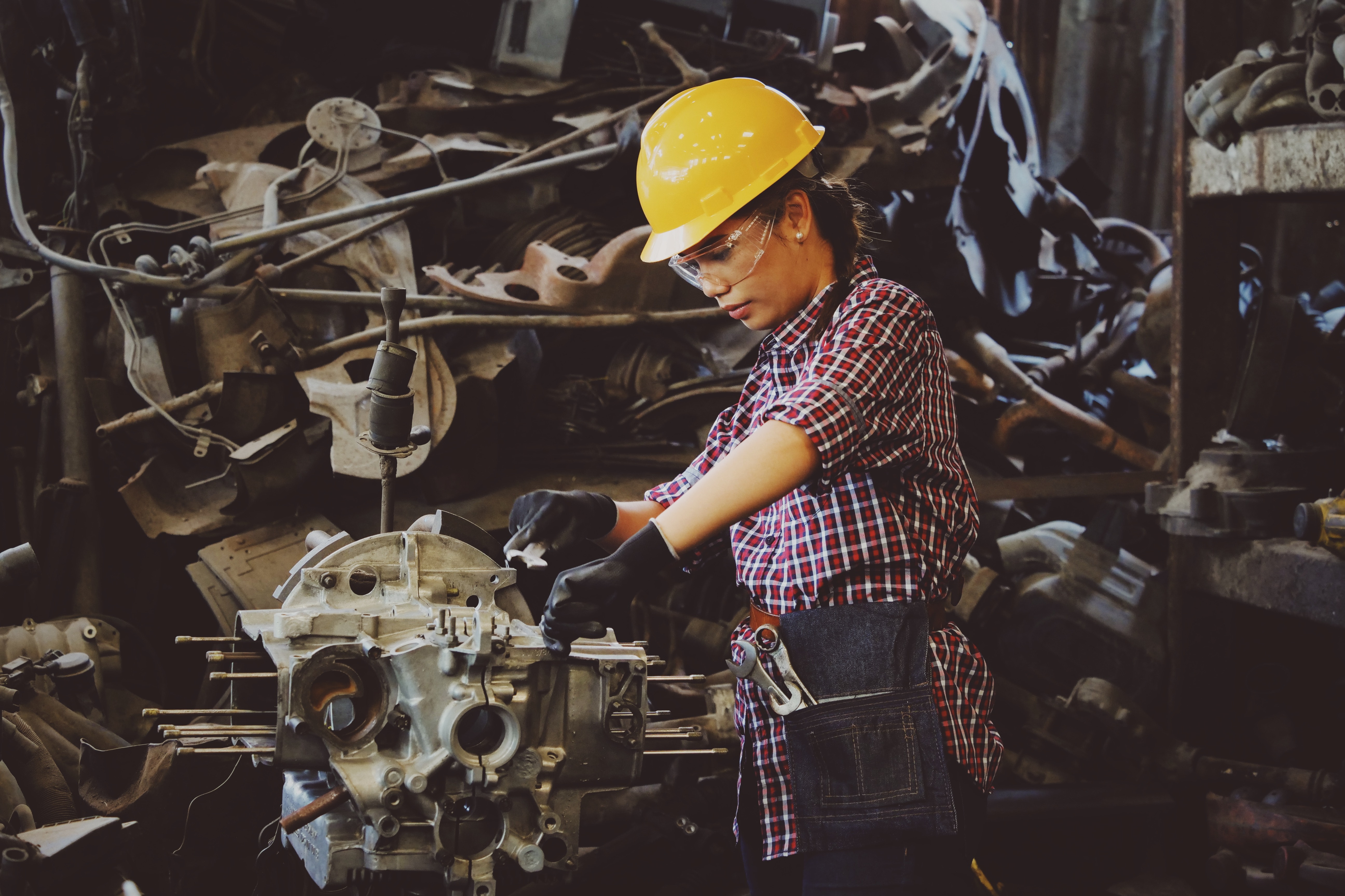 Mujer con casco amarillo y gafas, trabajando sobre un motor.