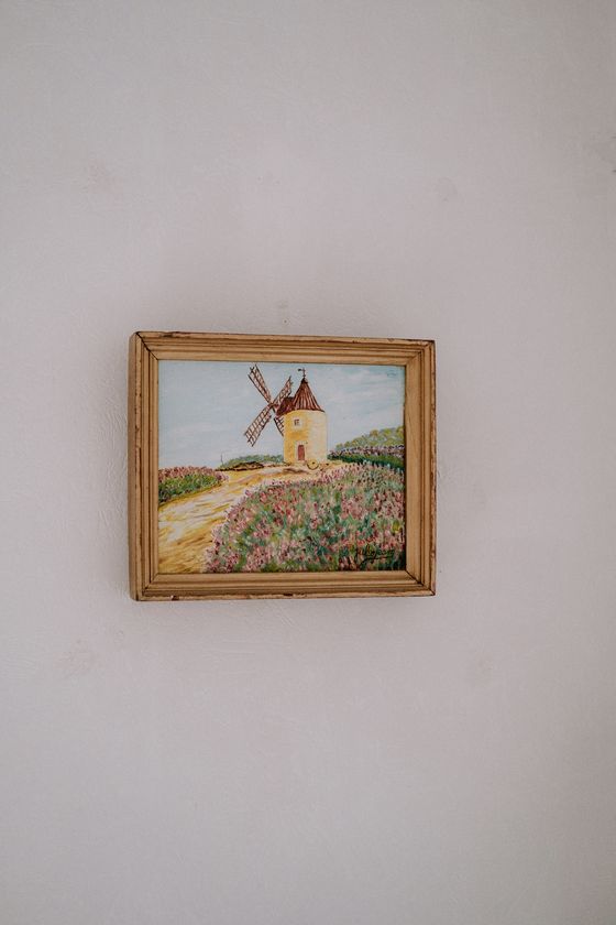 En la fotografía aparece un cuadro colgado en una pared. En el cuadro se aprecía un paisaje de un camino con un molino. El cuadro esta realizado con téncia de óleo.