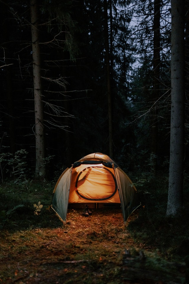La imagen muestra una tienda de campaña iluminada de noche en el bosque