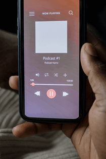 La imagen muestra una mano de una persona sosteniendo un teléfono móvil, en la pantalla se ve abierta la aplicación para grabar un podcast.