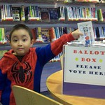 En la imagen puedes ver un niño disfrazado del hombre araña votando en una biblioteca pública a sus personajes de ficción favoritos