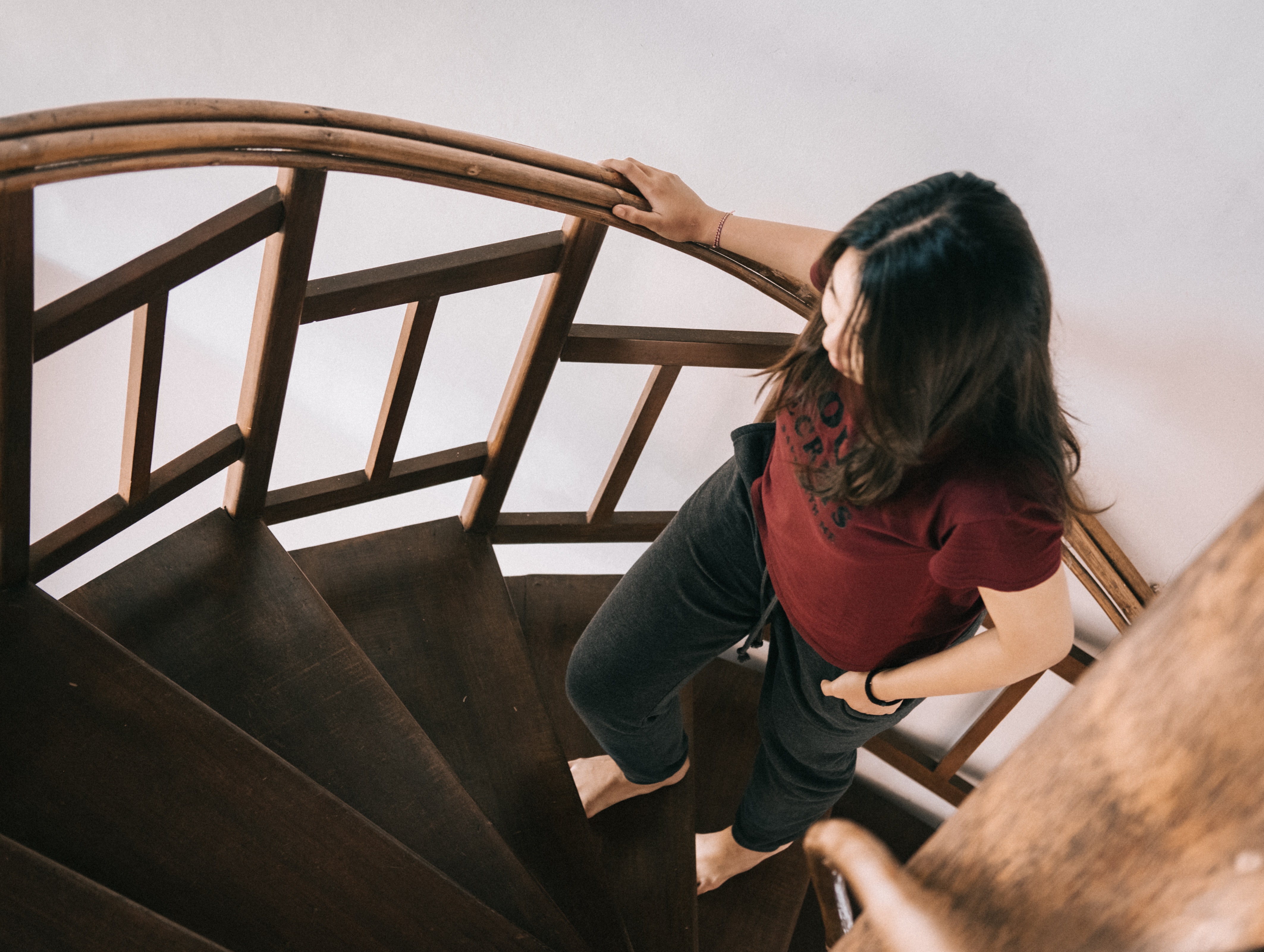 Fotografía vista desde arriba con una joven morena subiendo unas escaleras de madera en forma de caracol
