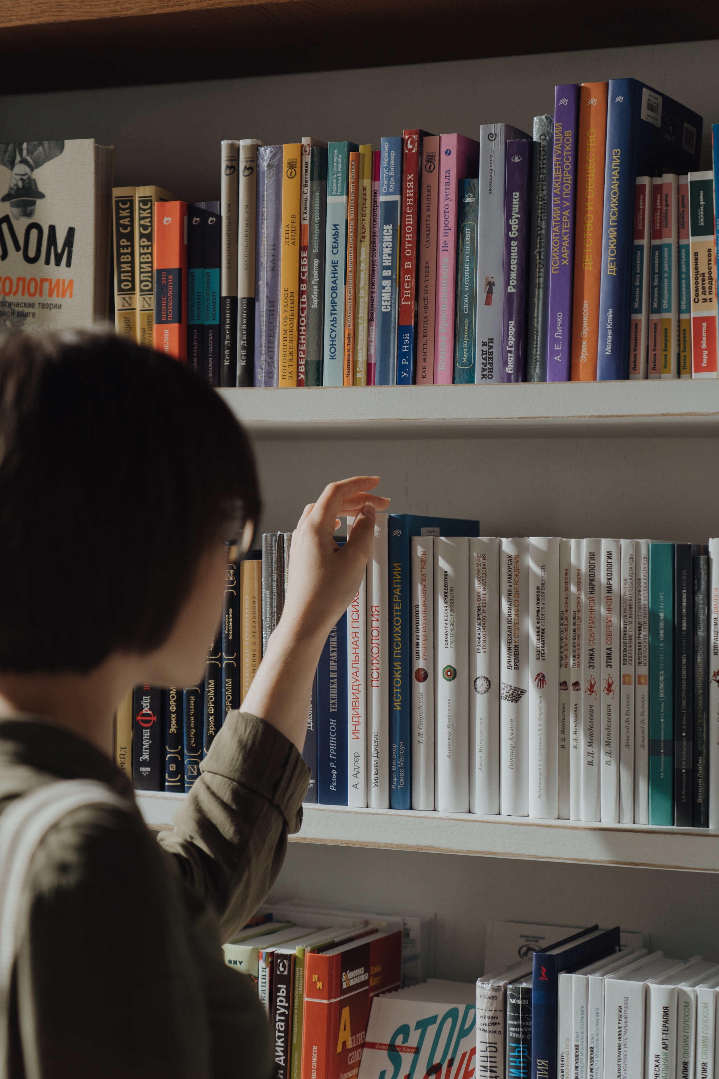 Una persona eligiendo un libro de una estateria de la biblioteca