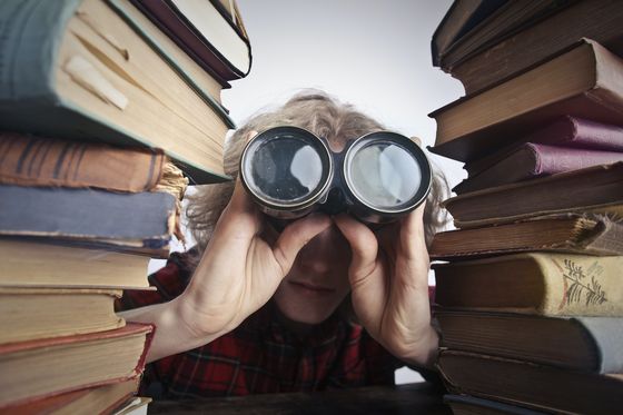 Fotografía con un niño observando a traves de unos prismáticos, a los lados aparecen dos montones de libros.