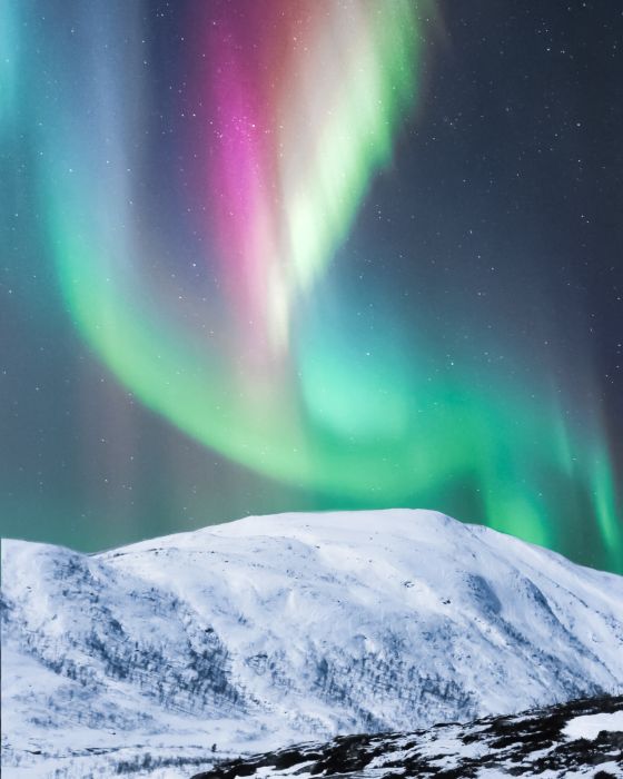 Imagen de luces polares de colores sobre montaña nevada.