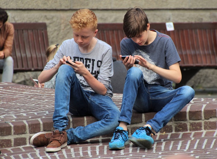 Dos chicos sentados en unos escalones, cada uno pendiente de sus dispositivos móviles.