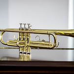 En la imagen puedes ver una trompeta dorada, sobre la tapa de un piano