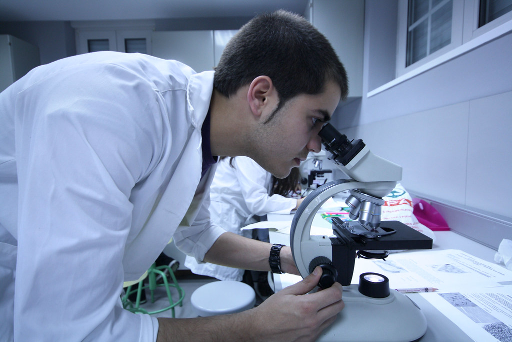 La imagen muestra un científico que mira atento por un microscopio